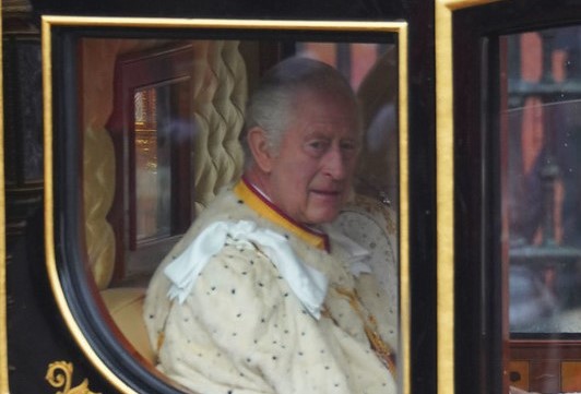 King Charles III sitting in a carriage in the coronation procession.