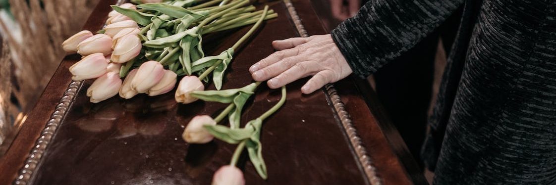 A person touches a coffin decorated with flowers.