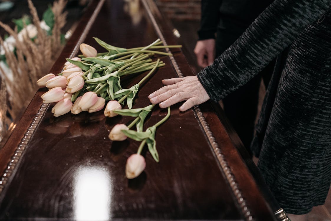 A person touches a coffin decorated with flowers.