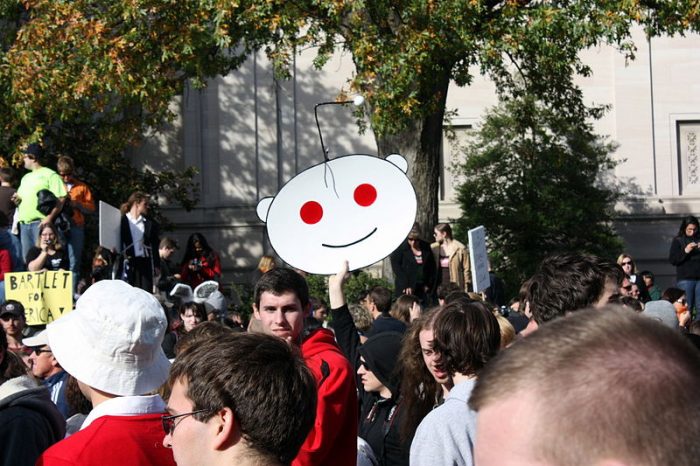 A person holding up a Reddit logo at a protest.