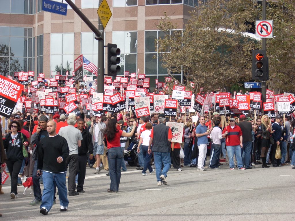 Workers marching with red and white signs during the Hollywood writers strike.