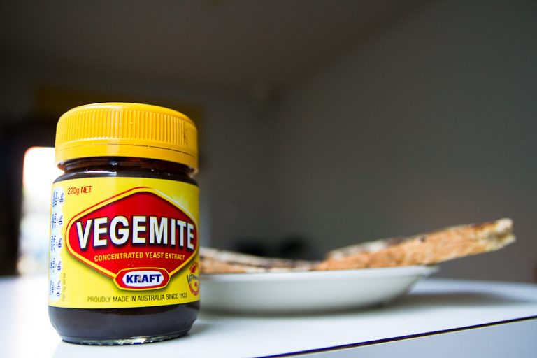 A jar of vegemite on a benchtop with toast in the background