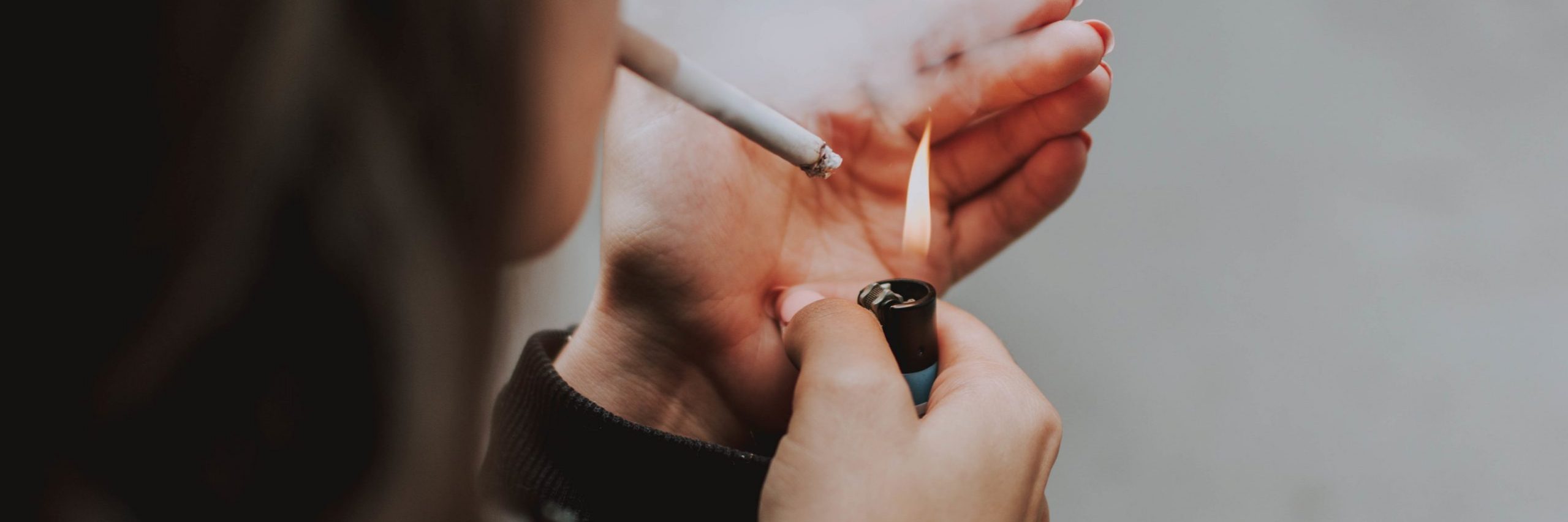 A selective closeup shot of a female lighting up a cigarette with a lighter