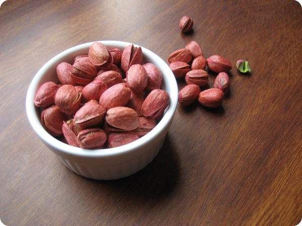 red pistachios in a bowl with some scattered on the table besides it