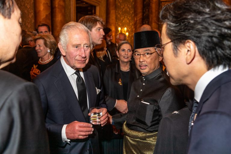 King Charles III conversing in a group with a drink.