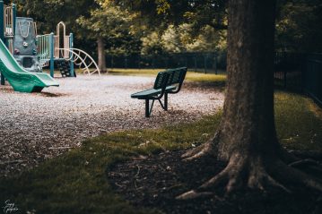 an empty park bench in daytime overlooking a deserted playground