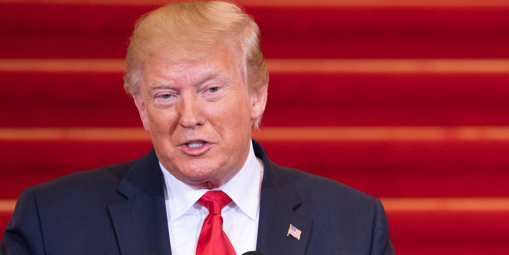 Trump standing with mic on stairs podium.