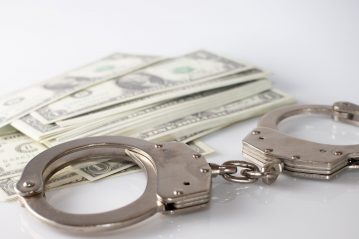 A high angle shot of metal handcuffs and some dollar bills, metaphorically representing the arrest of the accountant