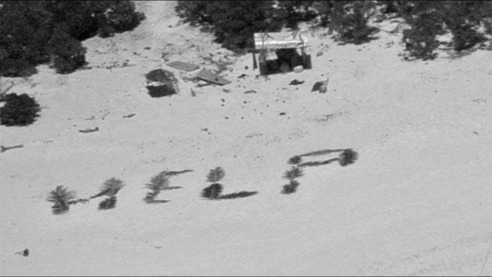 "Help" spelled out in palm leaves on the island shore.