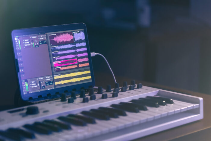Digital tablet screen showing the interface of a music program and piano keyboard, showing someone working with sound to record music. Image source: pvproductions, via Freepik
