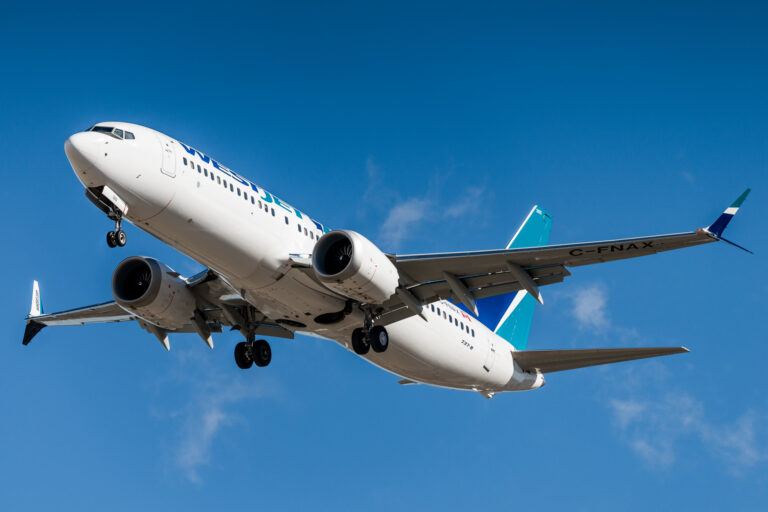 An image of a boeing 737 MAX in a blue sky. The plane is white with a blue tail. The company branding is obscured. Image source: AceYYC, via: Wikimedia Commons