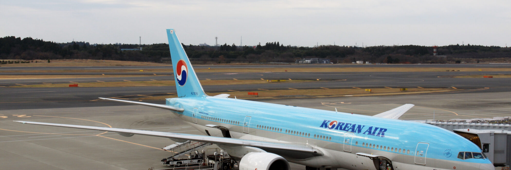 An image of a Korean Air aircraft parked on a runway at Narita International Airport. The airplane is pale blue on the top and white below, with the name 'Korean Air' on the side. Image source: Kentaro Iemoto, via Wikimedia Commons.