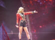 An image of Taylor Swift onstage, wearing a red jacket and holding a microphone. Image source: Jana Beamer, via Wikimedia Commons