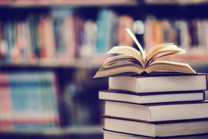 An image of an opened book on top of a stack of other books, with shelves full of other books behind them. Booktopia was often in competition with Amazon for trade. Image source: jcomp, via Freepik