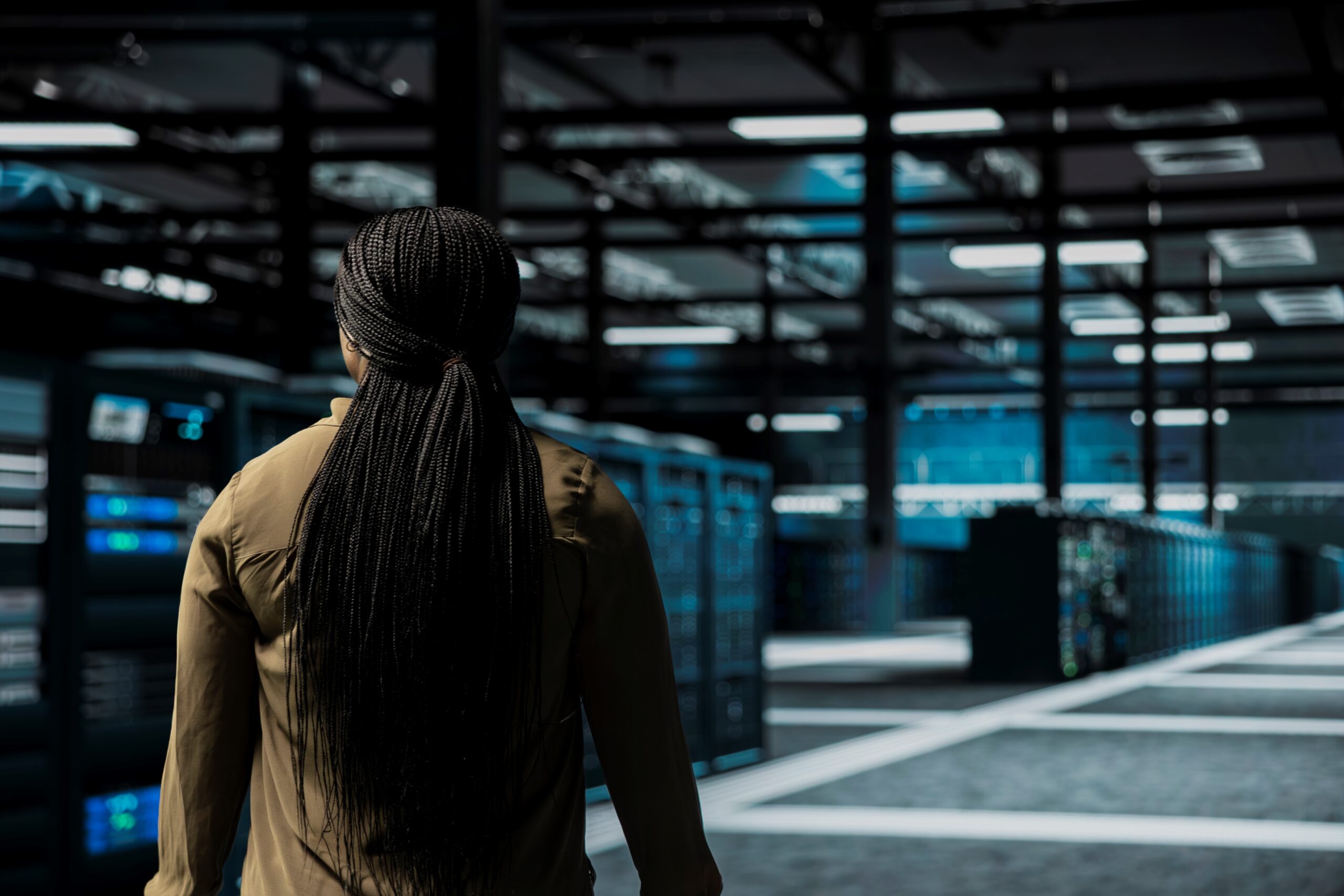 A software developer walks among server room rows lined with storage infrastructure rigs in a data centre. Photo: DC Studio on Freepik.