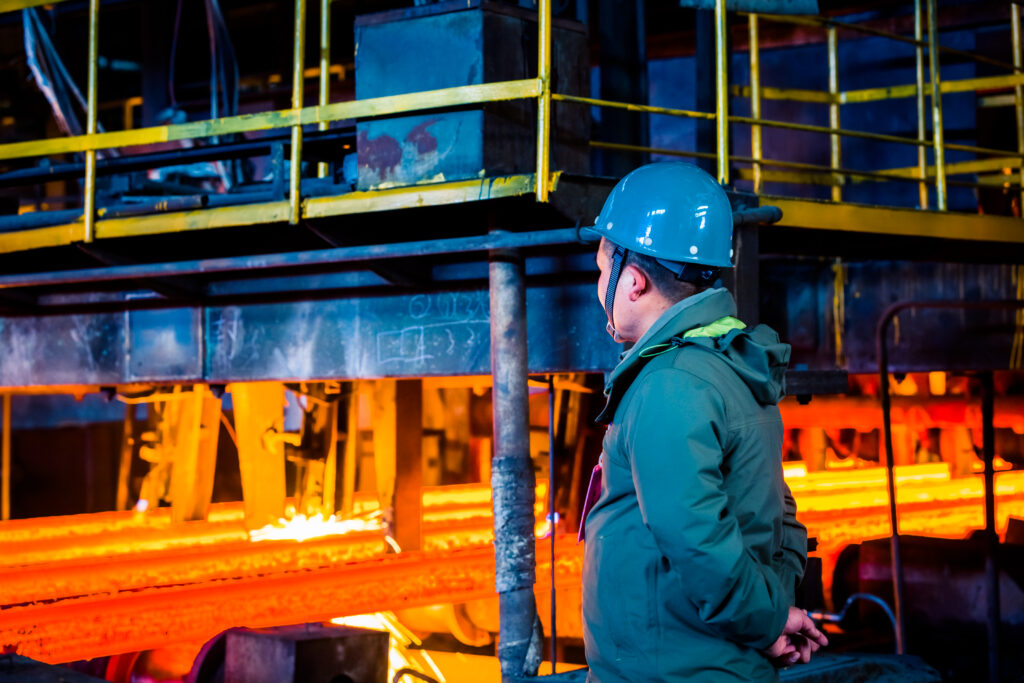 Worker in a hard hat watching glowing hot metal inside a heavy industrial plant, representing the Bell Bay Aluminium smelter in Tasmania