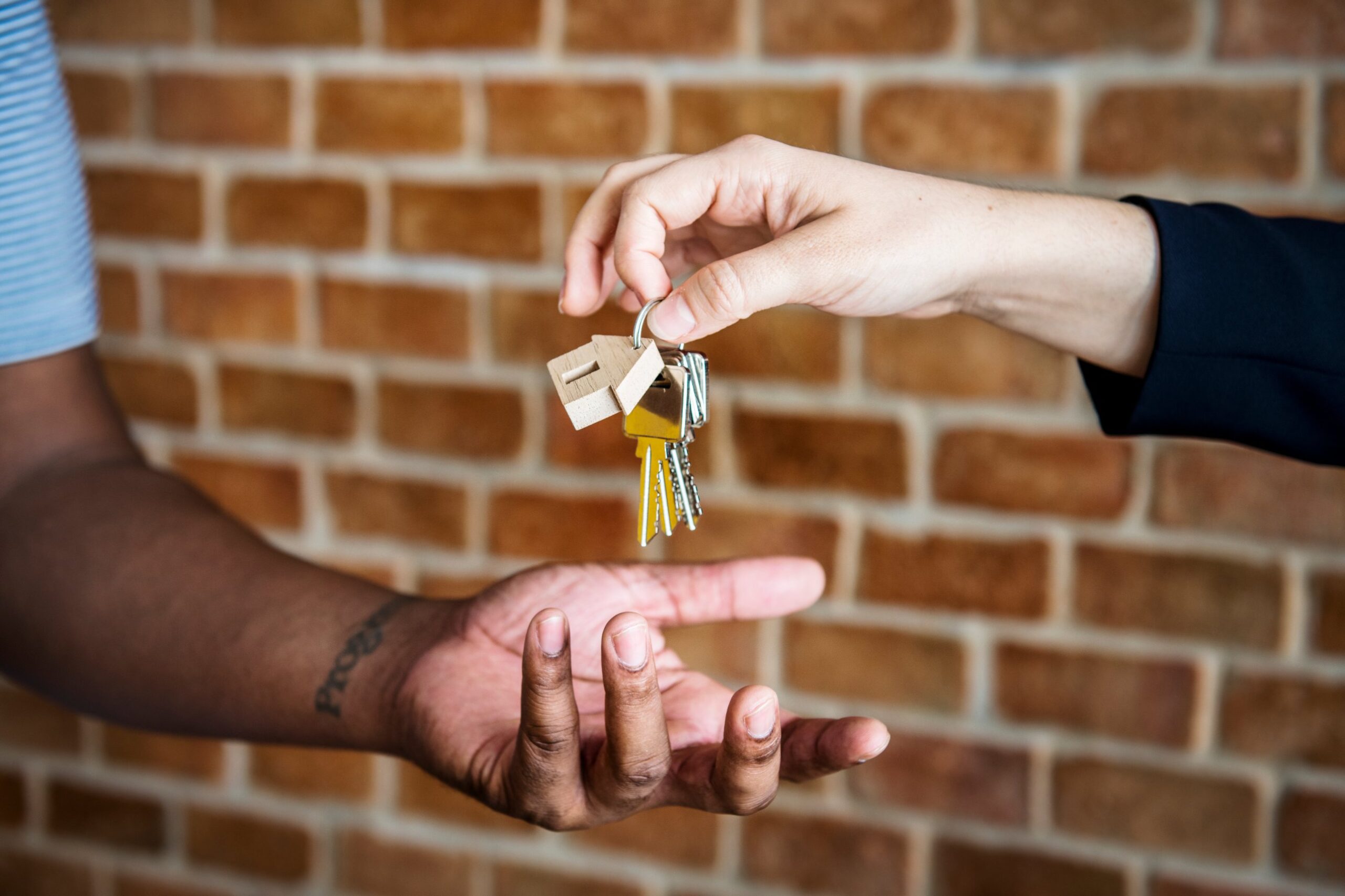 One hand passing a set of house keys with a wooden house tag to another, illustrating Smart Rental Bonds for renters moving home