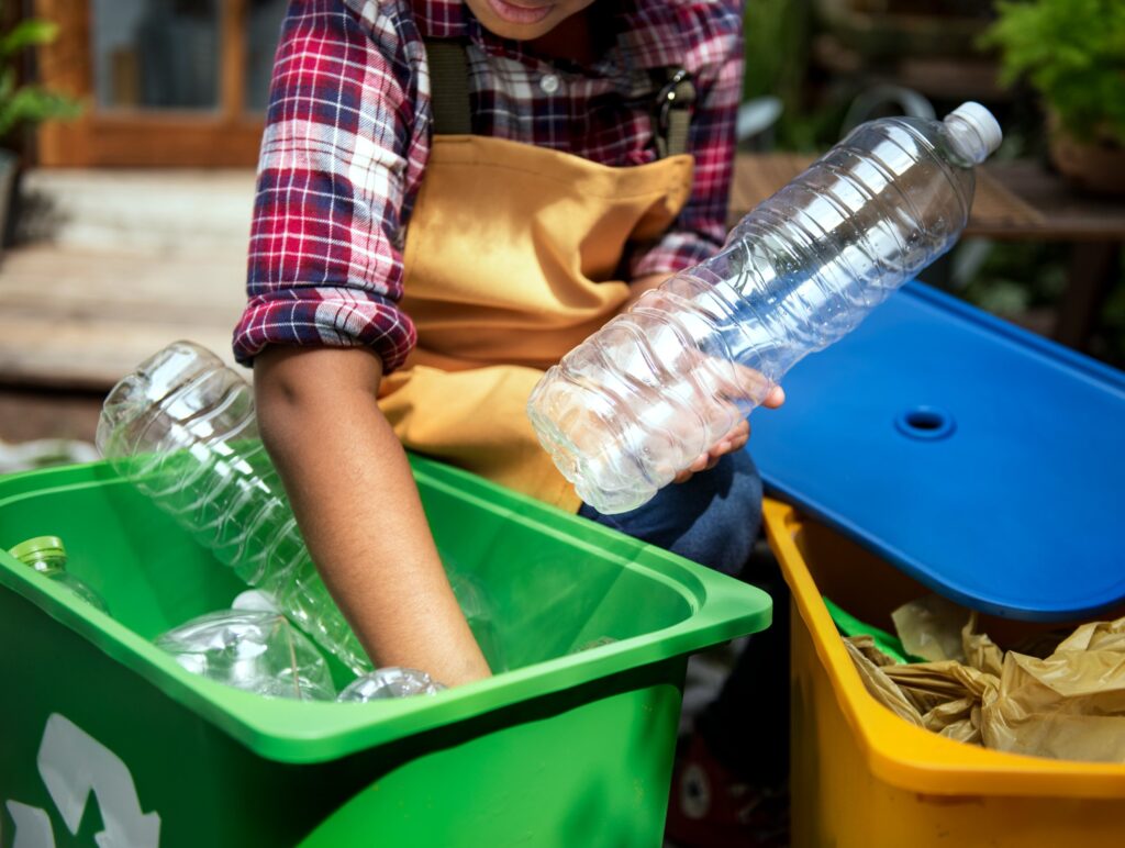 Person putting plastic bottles into a green recycling bin beside a yellow bin, illustrating Kiama recycling