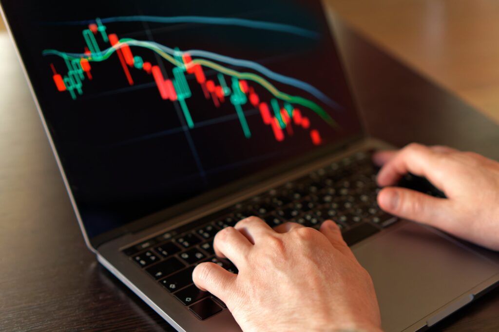 Hands typing on a laptop showing falling candlestick charts, CFD product intervention order