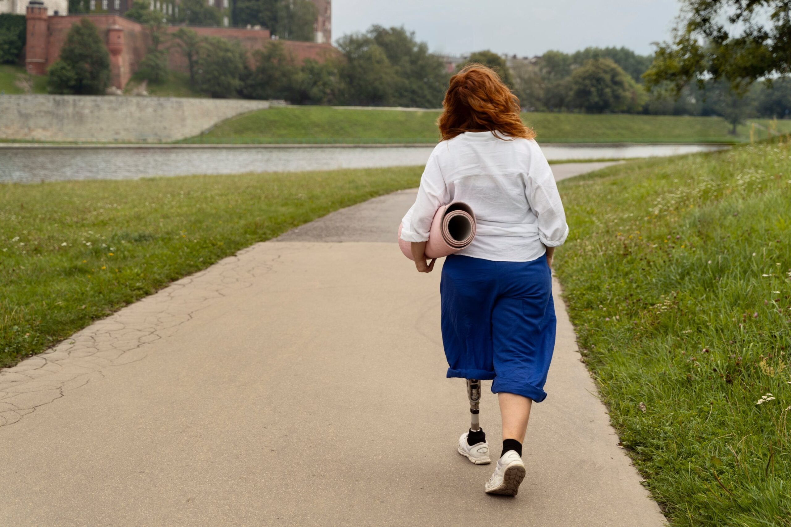 Woman with a prosthetic leg walking along a riverside path carrying a yoga mat, illustrating the NDIS reforms and support for people with disability
