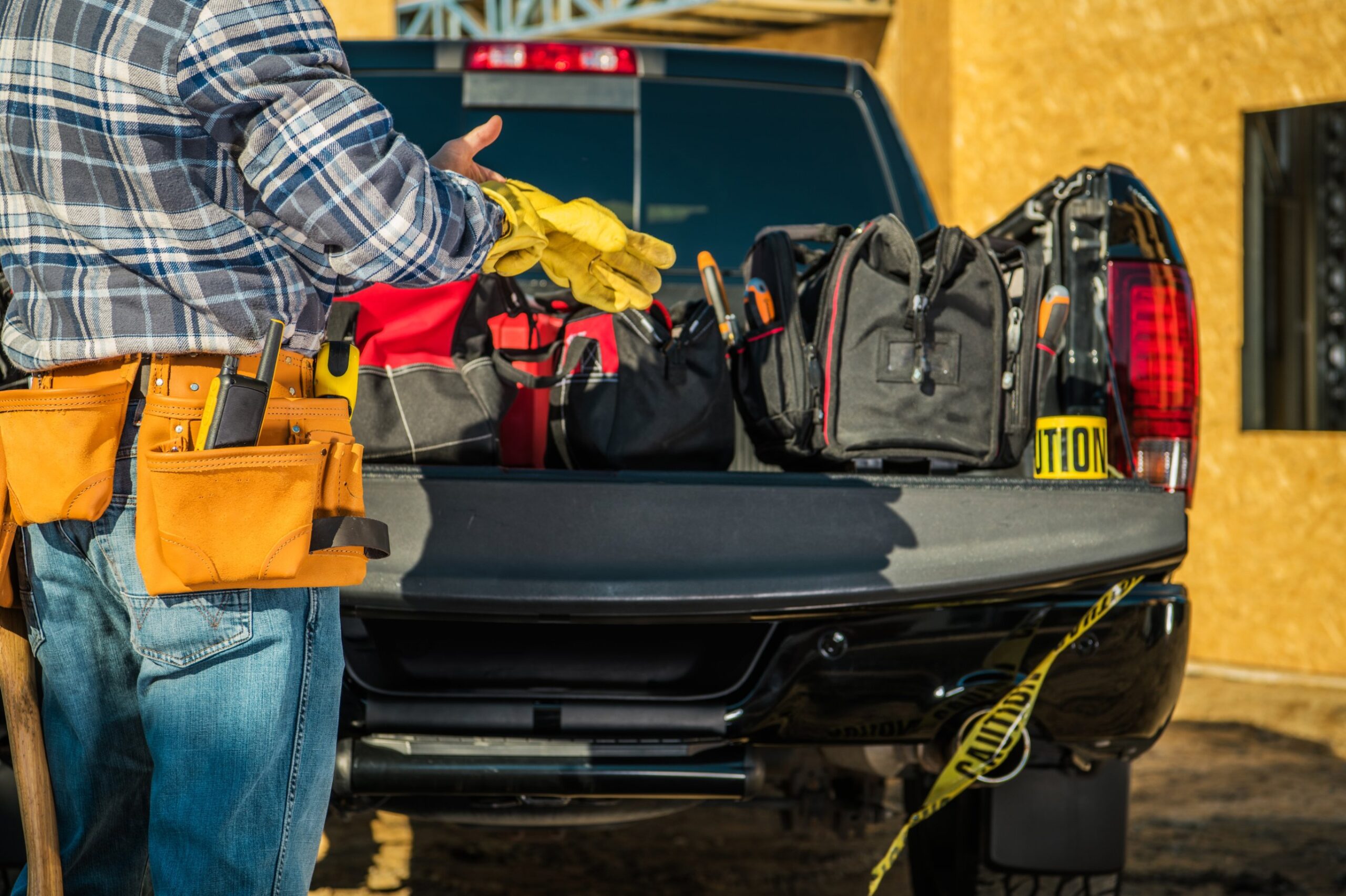 Tradie with tool belt and gloves beside tool bags on a ute, a focus for Queensland security grants
