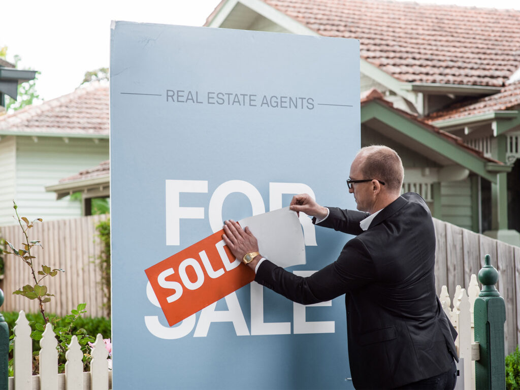 Real estate agent attaching a sold sticker to a for sale sign, property price disclosure rules Victoria