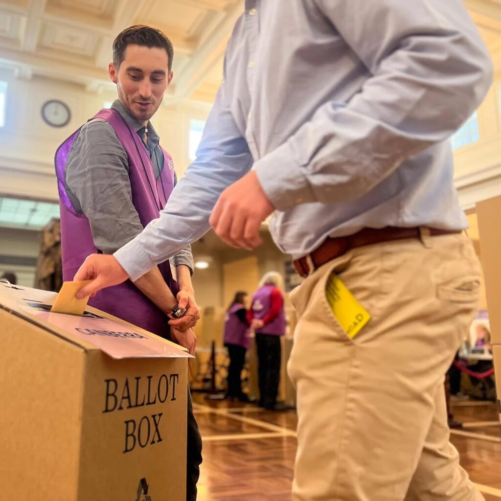 Voter placing a ballot paper in a ballot box at a polling place, illustrating WA local government reform